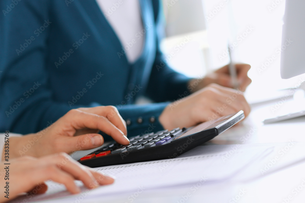 Accountant checking financial statement or counting by calculator income for tax form, hands closeup. Business woman sitting and working with colleague at the desk in office. Tax and Audit concept Accountant checking financial statement or counting by calculator income for tax form, hands closeup. Business woman sitting and working with colleague at the desk in office. Tax and Audit concept