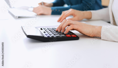 Accountant checking financial statement or counting by calculator income for tax form  hands closeup. Business woman sitting and working with colleague at the desk in office. Tax and Audit concept