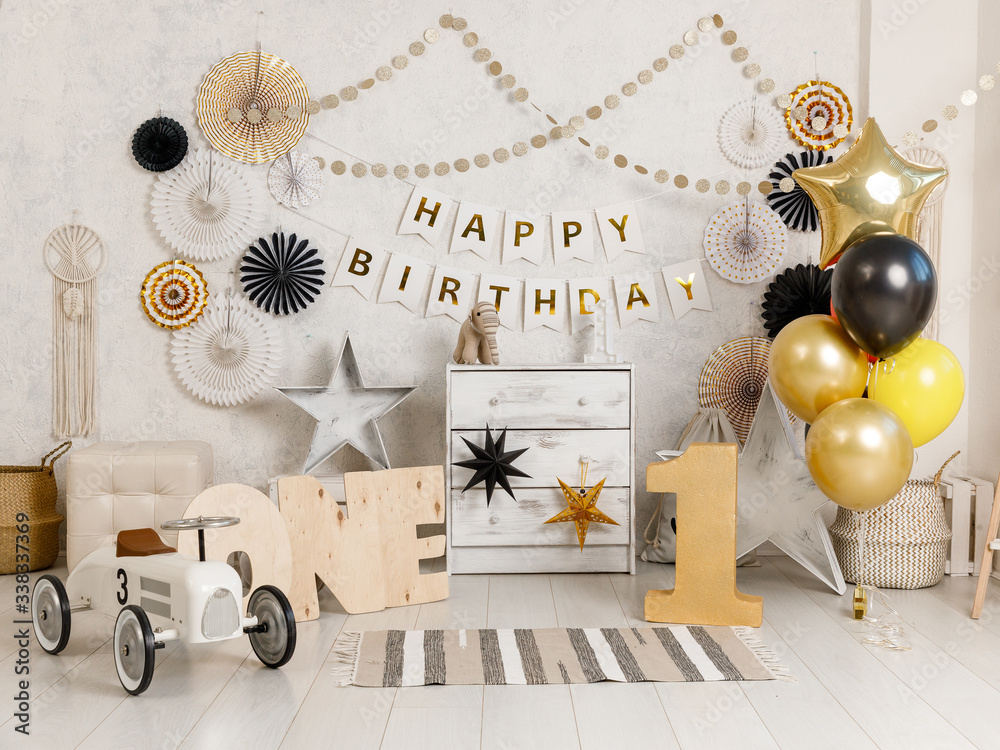 Birthday decorations with balloons, gifts, toys, garlands and candy for  yearling, little baby party, celebration on a white wall background. Black  and gold Decor elements. Stock Photo