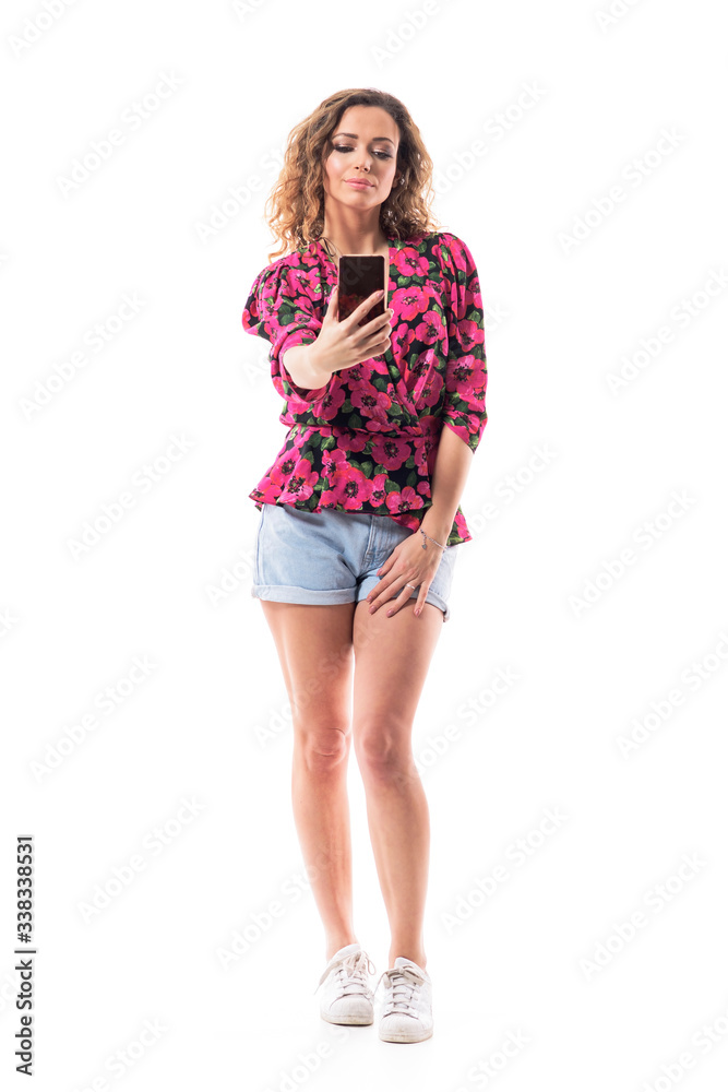 Confident stylish young woman in summer clothes with curly hair taking selfie or photos with cell phone. Full body isolated on white background. Confident stylish young woman in summer clothes with curly hair taking selfie or photos with cell phone. Full body isolated on white background.