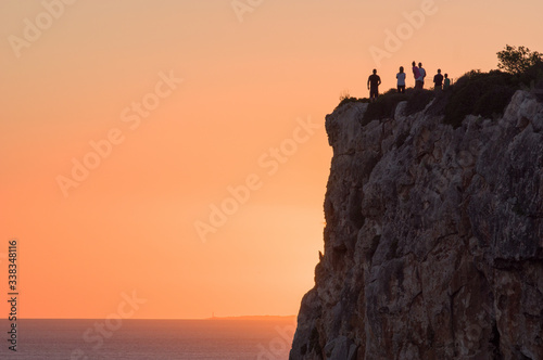 People watching pretty sunset over cliffs and sea in Menorca, Spain