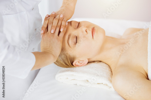 Beautiful caucasian woman enjoying facial massage with closed eyes in sunny spa salon. Relaxing treatment in medicine and Beauty concept