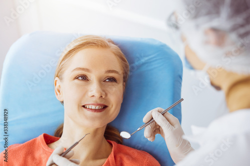 Smiling caucasian woman is being examined by dentist at sunny dental clinic. Healthy teeth and medicine  stomatology concept