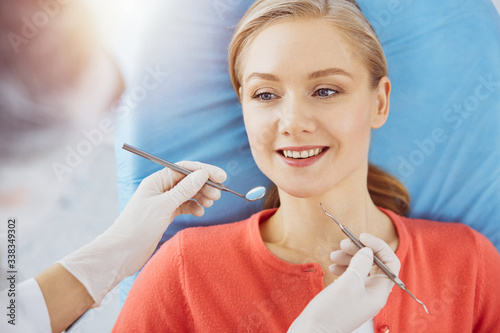 Smiling caucasian woman is being examined by dentist at sunny dental clinic. Healthy teeth and medicine, stomatology concept