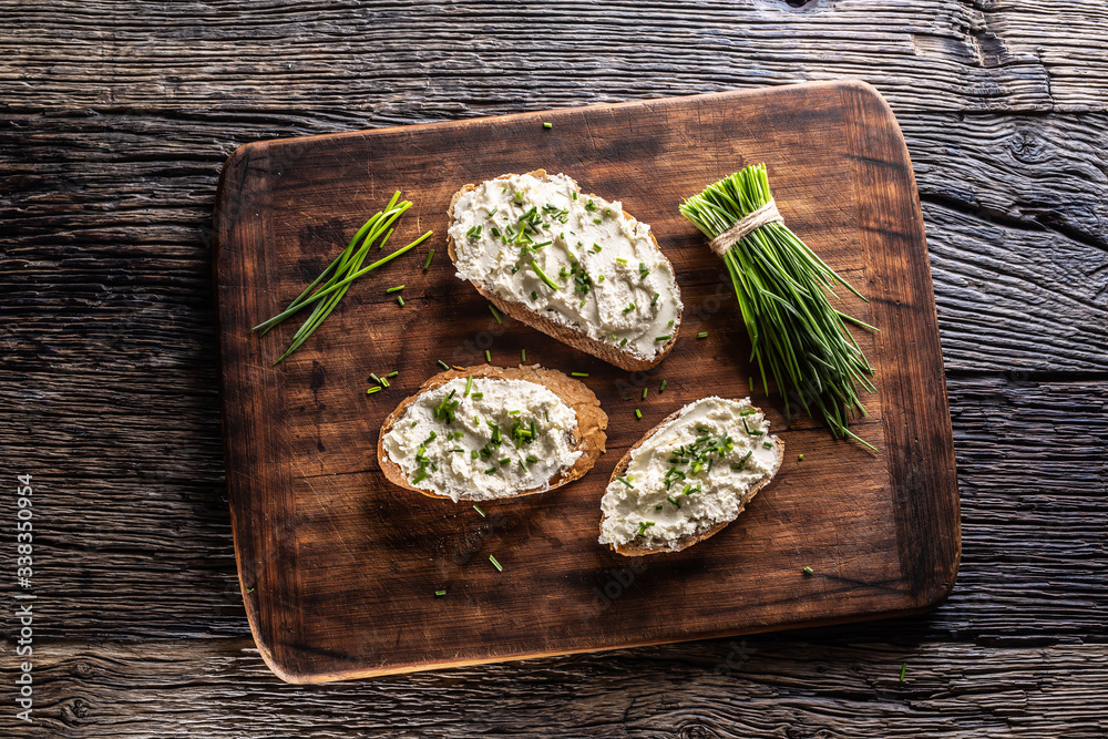 Slices of bread with a cottage cheese spread, freshly cut chives, and a bunch of chive aside placed on a dark brown cutting board and vintage background - obrazy, fototapety, plakaty 