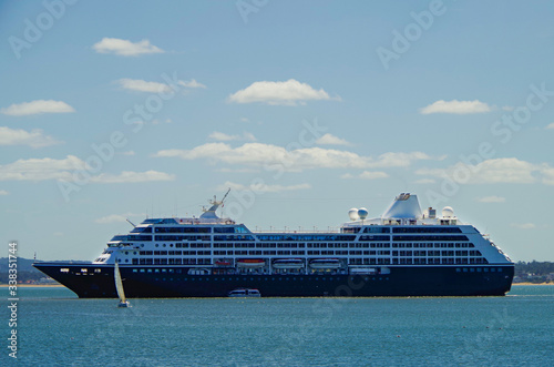 Luxury cruiseship or cruise ship vessel Azamara Pursuit anchors at sea with sailing boat or yacht during summer with sky and clouds photo