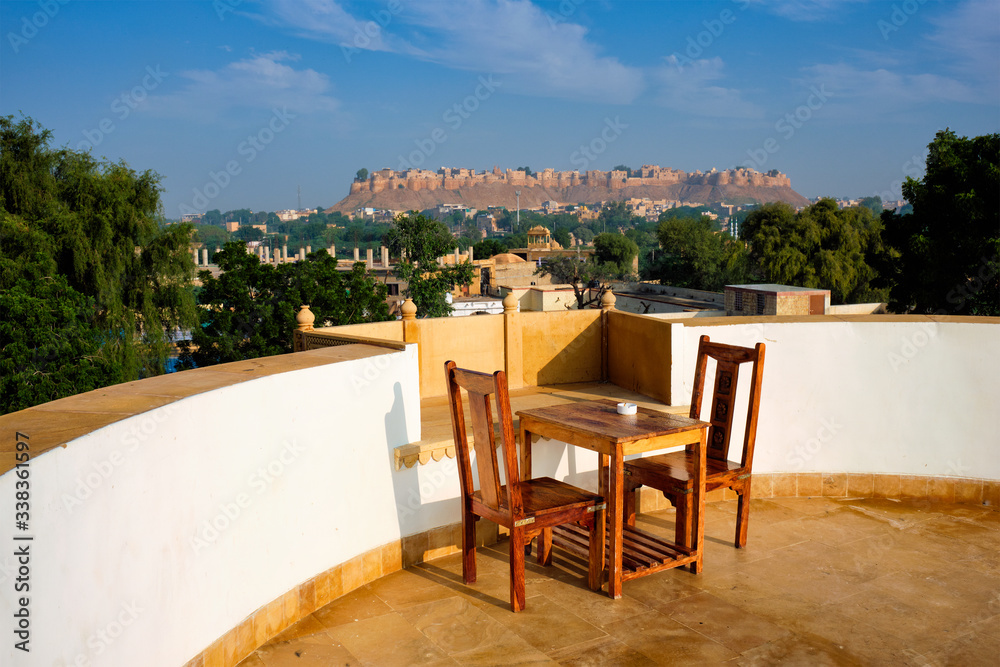 Fototapeta premium Rooftop Table with chairs with view of tourist landmark of Rajasthan - Jaisalmer Fort known as the Golden Fort Sonar quila, Jaisalmer, Rajasthan, India