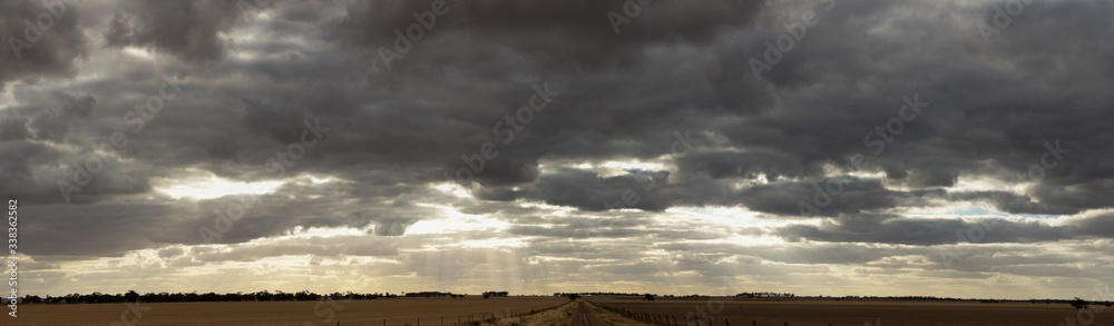 panoramic of a dramatic cloud filled late afternoon sky stretching over large farm fields in rural Victoria just after harvest with a dirt road down the middle.