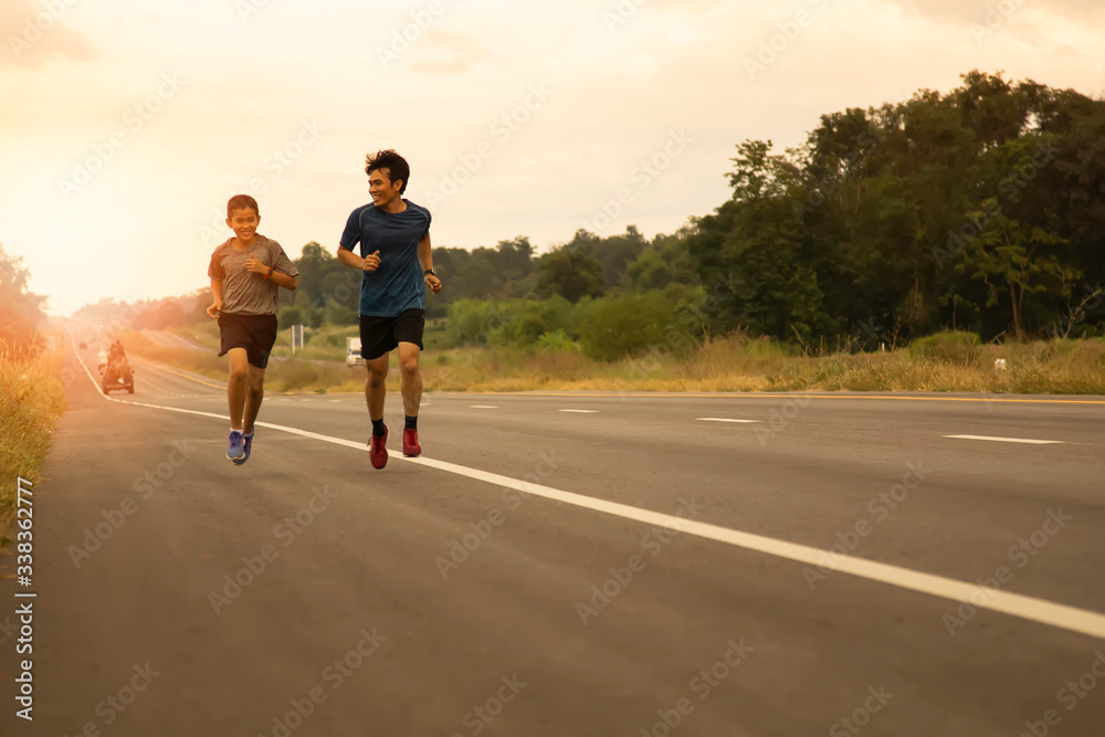Father and son come to jogging in the evening on the public road on a holiday with the orange light of the sun coming from behind, leisure activities that make the body healthy Father and son come to jogging in the evening on the public road on a holiday with the orange light of the sun coming from behind, leisure activities that make the body healthy