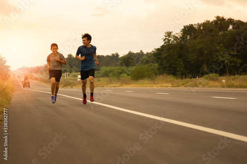 Father and son come to jogging in the evening on the public road on a holiday with the orange light of the sun coming from behind, leisure activities that make the body healthy