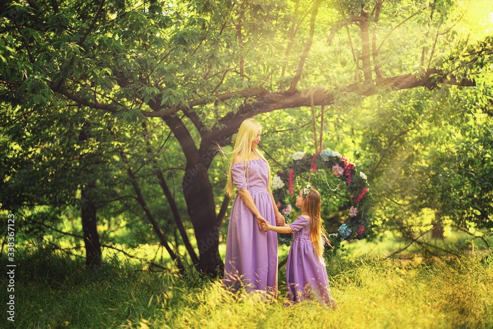 Fototapeta premium fashion outdoor photo of beautiful family look. beautiful mother with long blonde hair posing and playing with her daughter in similar lavender dresses in the park outdoor