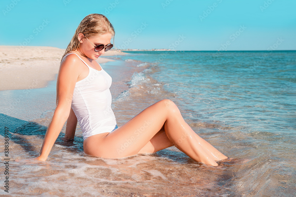 Beautiful girl sunbathing on a sandy tropical beach. Fashion young female lying on back on sand with white swimsuit. Tanned blonde woman relaxing Beautiful girl sunbathing on a sandy tropical beach. Fashion young female lying on back on sand with white swimsuit. Tanned blonde woman relaxing