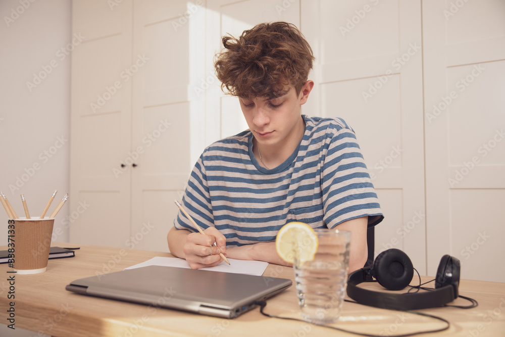 A smiling teenage boy learns at his desk in his room. Distance learning because of the epidemic coronavirus A smiling teenage boy learns at his desk in his room. Distance learning because of the epidemic coronavirus