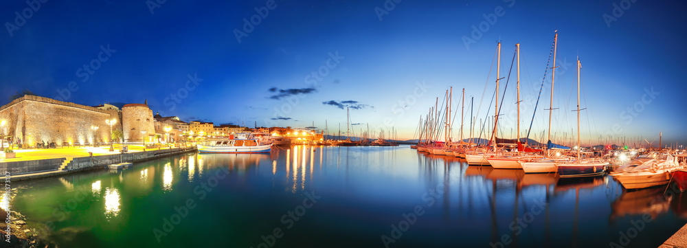 Night view of the Alghero Marina yacht port at the Gulf of Alghero with anchored sailboats