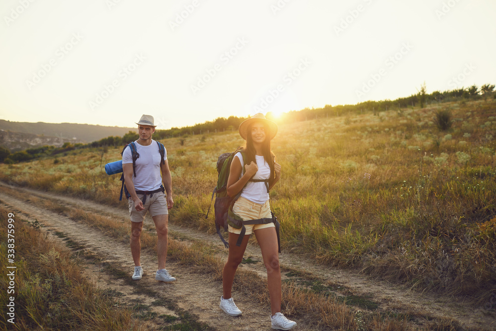 Hiking couple with backpack walking on hike in nature at sunset with the sun.