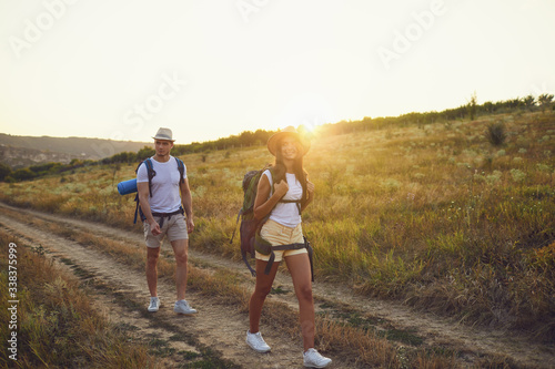 Hiking couple with backpack walking on hike in nature at sunset with the sun.