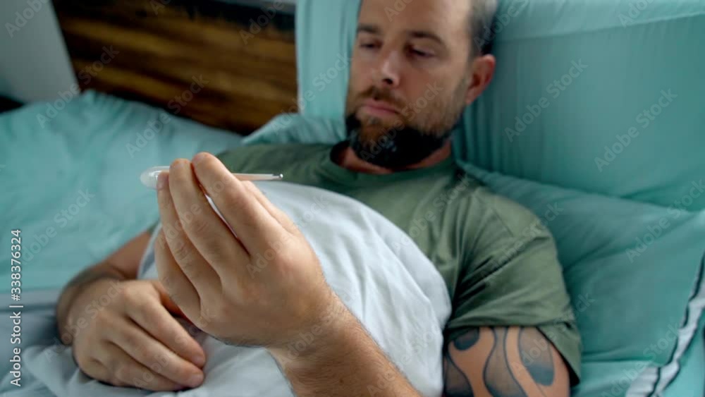 Man laying in bed being sick checking his temperature Man laying in bed being sick checking his temperature