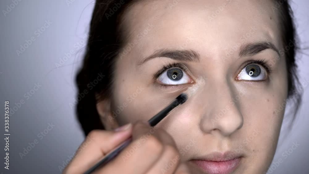 Process of Professional Makeup for beautiful and gorgeous woman sitting at the Studio. Make up Artist applies concealer on eyes area Process of Professional Makeup for beautiful and gorgeous woman sitting at the Studio. Make up Artist applies concealer on eyes area