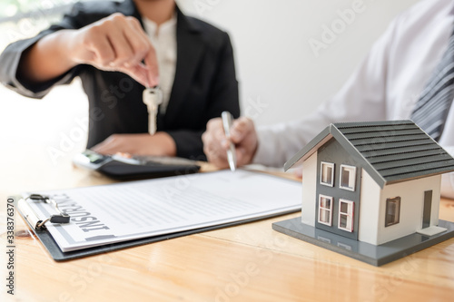 Real estate agent broker hand over the house key to the new owner after completing the signing according to agreement renting a house and buy house insurance Home insurance concept
