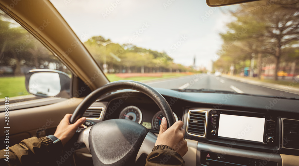 Naklejka premium People hands holding steering wheel while driving car on city road