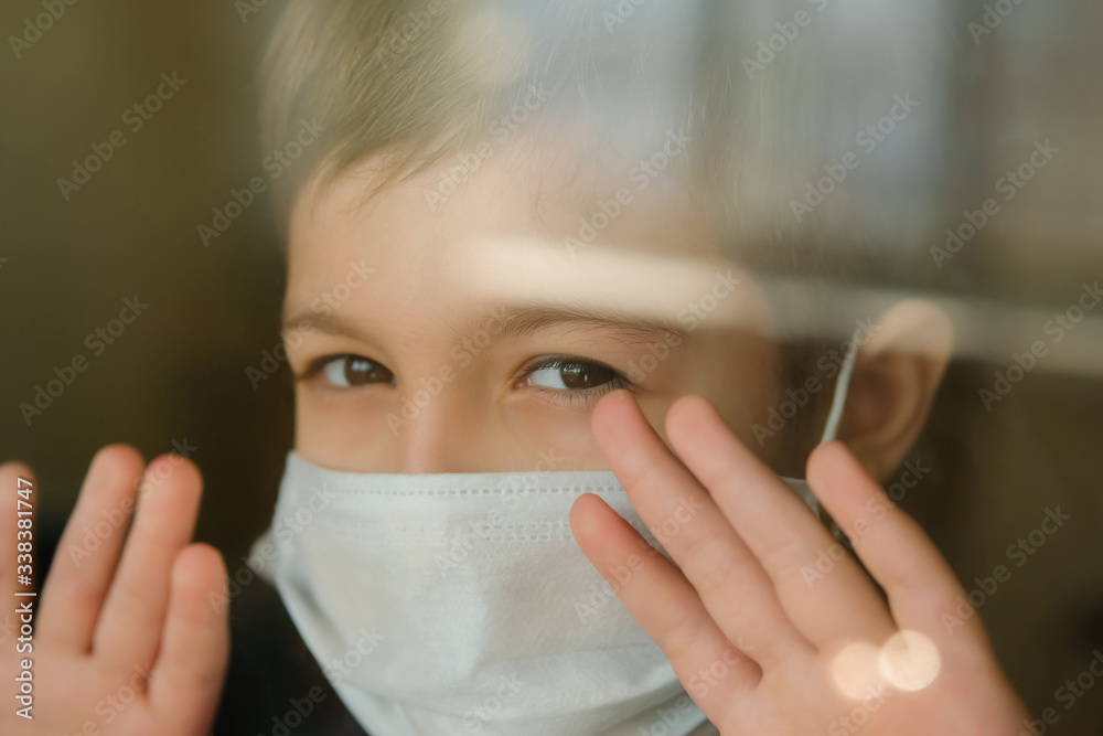 Young boy in a medical mask looks out the window. Self-isolation in quarantine, coronavirus, covid 19. Young boy in a medical mask looks out the window. Self-isolation in quarantine, coronavirus, covid 19.
