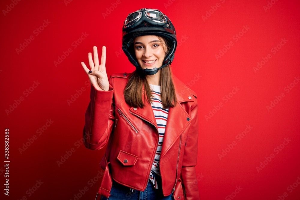 Young beautiful brunette motocyclist woman wearing motorcycle helmet and red jacket showing and pointing up with fingers number four while smiling confident and happy. Young beautiful brunette motocyclist woman wearing motorcycle helmet and red jacket showing and pointing up with fingers number four while smiling confident and happy.