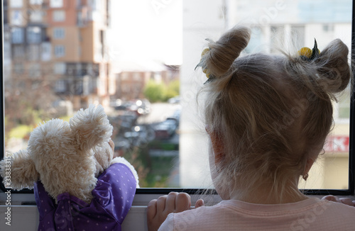 a small  girl with a stuffed toy looks out the window at the street