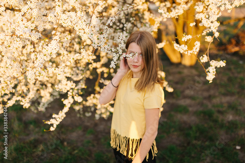 Portrait of young beautiful blonde woman near blooming tree with white flowers on a sunny day. Spring, girl near a flowering tree.beautiful girl in a yellow t-shirt near a flowering tree