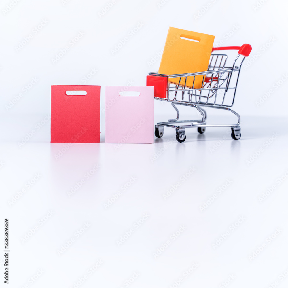 Shopping bags in a silver red shopping cart isolated on white table background, concept of staying home order, close up, copy space design.