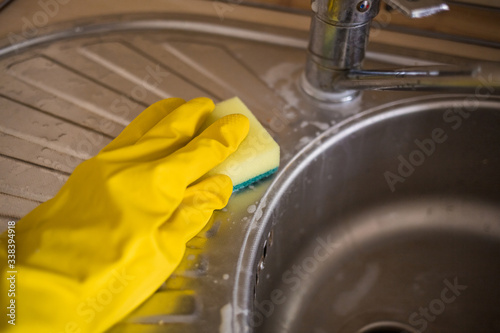 Tidying up. Wash the sink in gloves with a sponge. yellow gloves and a sponge. Household products for kitchen washing