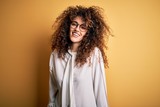 Young beautiful brunette woman with curly hair and piercing wearing shirt and glasses with a happy and cool smile on face. Lucky person.