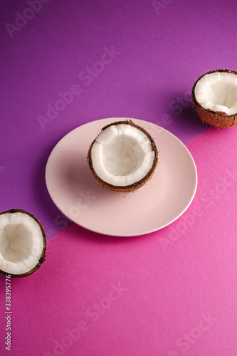 Coconut half in pink plate with nut fruits on violet and purple plain background  abstract food tropical concept  angle view