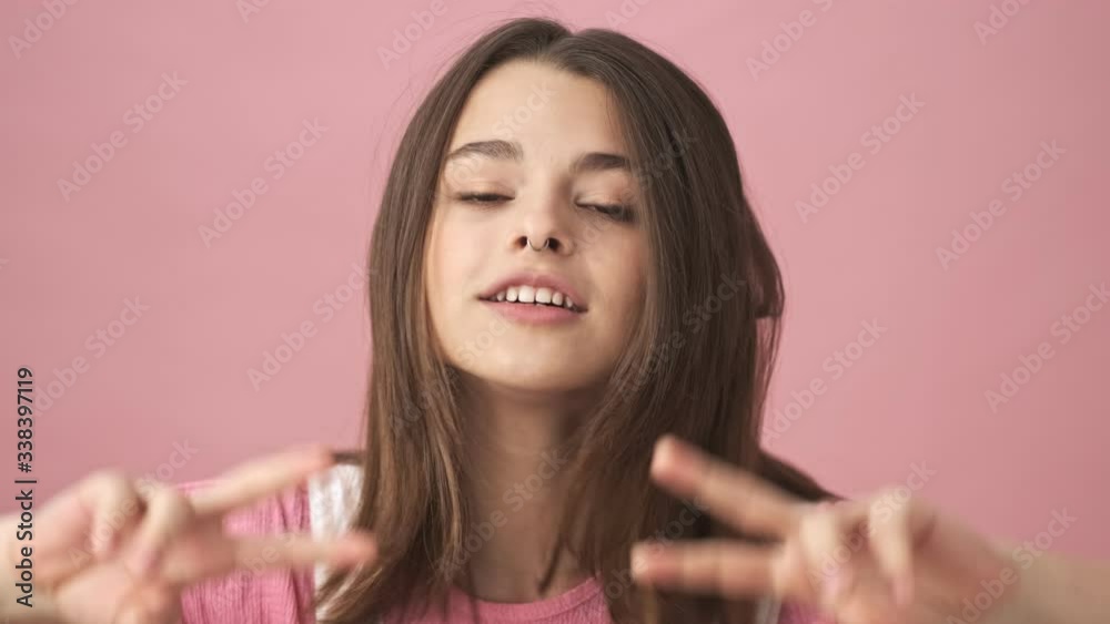 Joyful pretty brunette woman in overalls having fun and showing peace gestures over pink background Joyful pretty brunette woman in overalls having fun and showing peace gestures over pink background