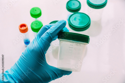 hand in a blue sterile glove holds a empty plastic container for collecting analyzes, white background