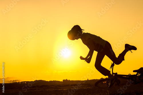 Silhouette of falling boy from bicycle, teenager was making trick on bycicle, silhouette of falling person at sunset in nature