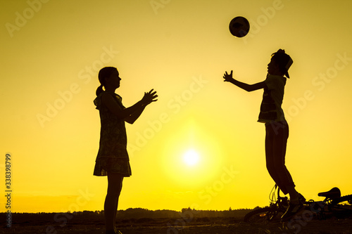 Brother with sister are playing with ball in nature, bicycle lies nearby, silhouettes of playing children at sunset in countryside