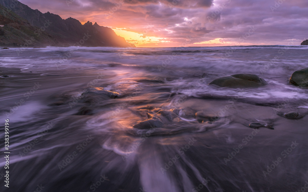 Meereswellen ziehen spuren über die Sandbank mit Sonnenuntergang im Hintergrund 
