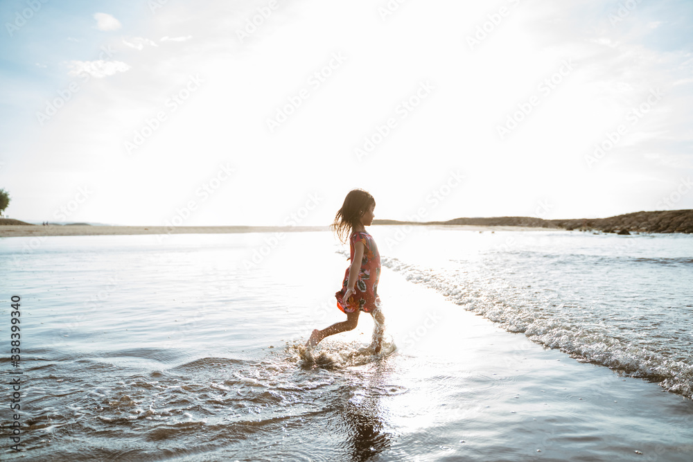 Little girl running on the beach while playing water on a beautiful beach