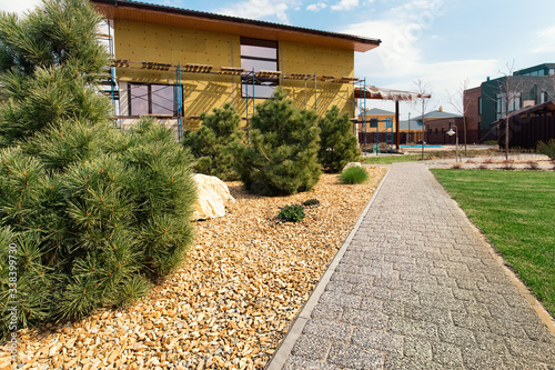 Modern  conifer tree garden design. House under construction. Pavement path of the garden