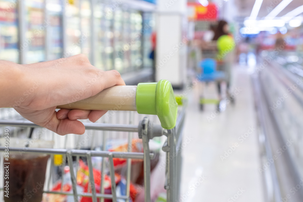 Woman hand holding shopping cart in super market or  convenience store concept and shelves in frozen food corner on blurry for background