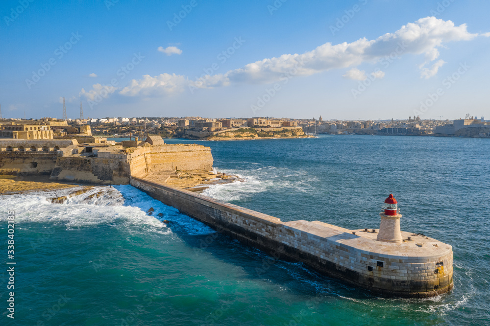 Aerial top view of red lighthouse and Fort Ricasoli East Breakwater. Big stormy waves, Mediterranean sea. Malta island
