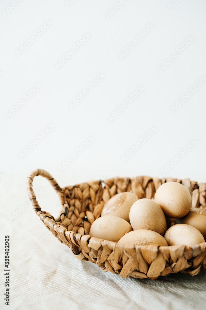 a natural basket with Easter eggs in a pastel brown color and with cracks stands on a white table.Easter concept.Minimal style. copy space for text