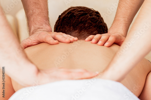 Young man receiving back massage in four hands in spa beauty salon.