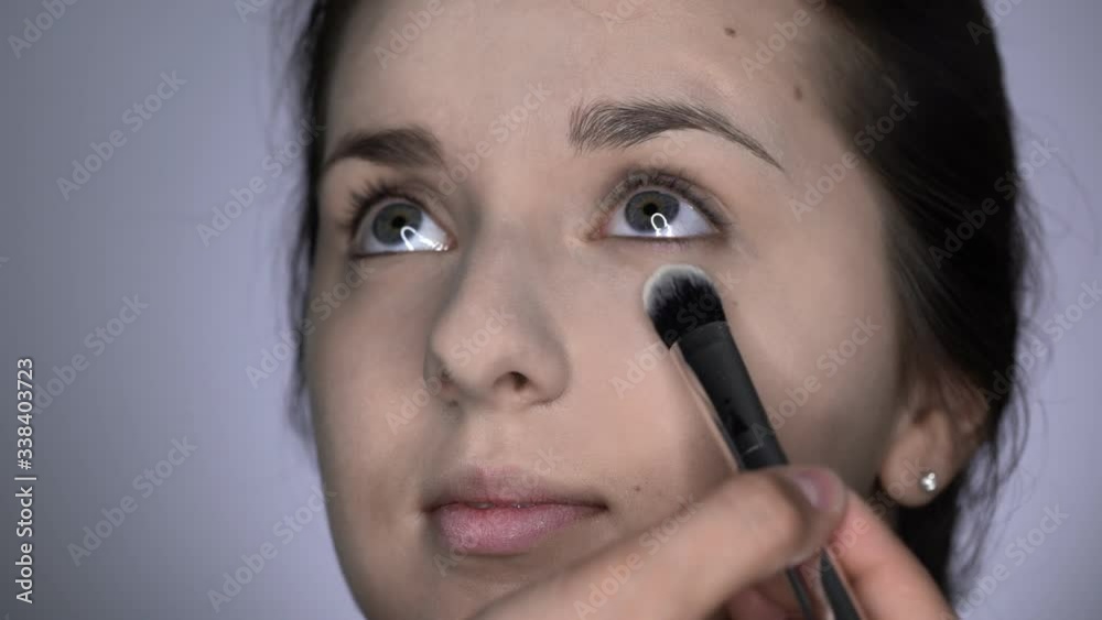 Process of Professional Makeup for beautiful and gorgeous woman sitting at the Studio. Make up Artist applies powder with a big brush on eyes area