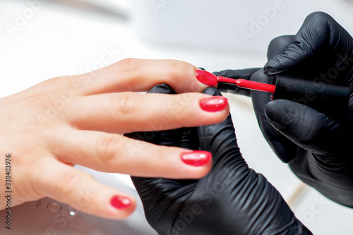 Manicurist paints fingernails with red nail polish in salon close up.