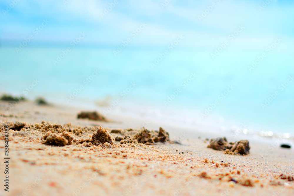 Summer background of tropical beach rest at the seaside, closeup of sand and blurred turquoise sea at sunny day Summer background of tropical beach rest at the seaside, closeup of sand and blurred turquoise sea at sunny day