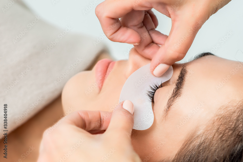 Hands of cosmetologist puts strip under eye of young woman before eyelash extension procedure. Hands of cosmetologist puts strip under eye of young woman before eyelash extension procedure.