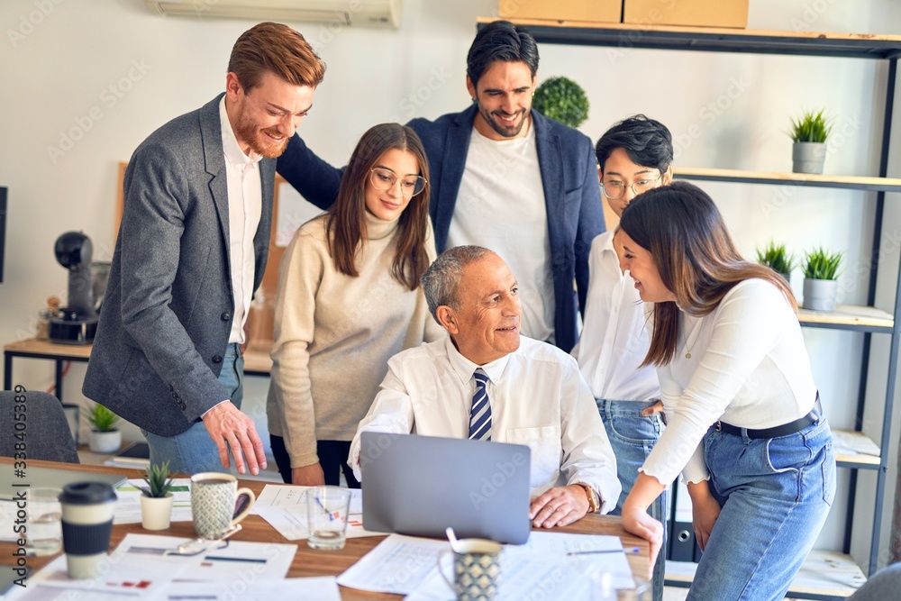 Group of business workers smiling happy and confident. One of them sitting and partners standing around. Working together with smile on face looking at the laptop at the office Group of business workers smiling happy and confident. One of them sitting and partners standing around. Working together with smile on face looking at the laptop at the office