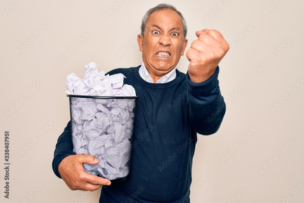 Senior grey-haired man holding full paper bin with crumpled papers over white background annoyed and frustrated shouting with anger, crazy and yelling with raised hand, anger concept Senior grey-haired man holding full paper bin with crumpled papers over white background annoyed and frustrated shouting with anger, crazy and yelling with raised hand, anger concept