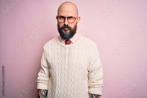 Handsome bald man with beard and tattoo wearing glasses and sweater over pink background skeptic and nervous, frowning upset because of problem. Negative person.